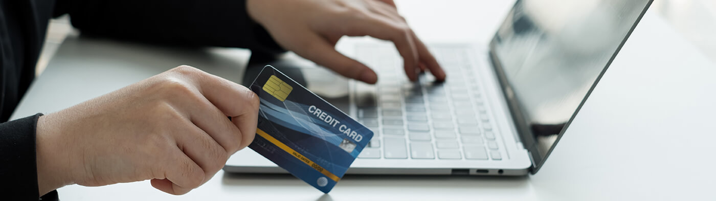 Close up of males hand holding credit card in front of laptop computer